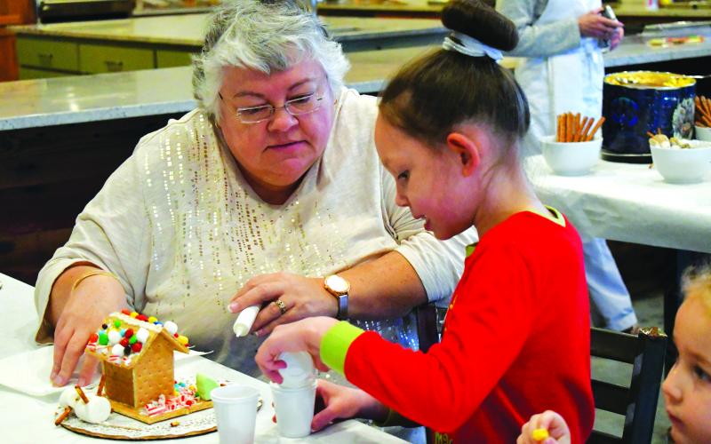 Enoch Autry/The Clayton Tribune. Teresia Dunn assists Estella Joy Chastain with a gingerbread house.