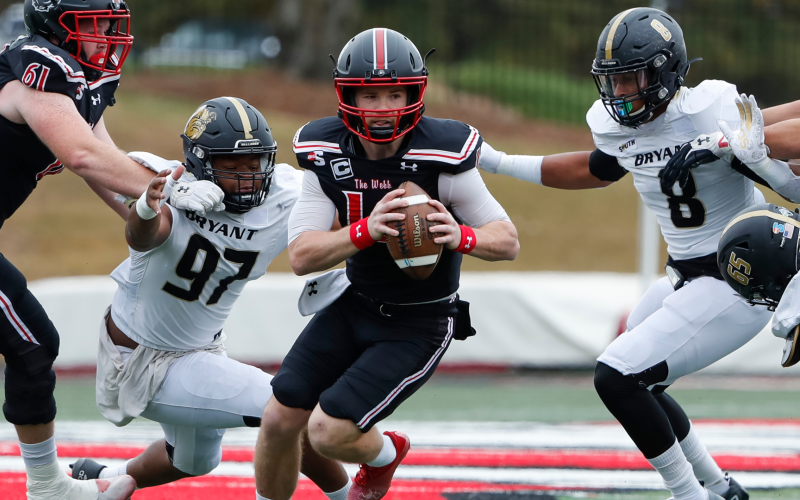 Courtesy of Gardner-Webb Athletics. Gardner-Webb redshirt senior Bailey Fisher evades two tackles in a game against Bryant on Oct. 29. Fisher, a former Rabun County Wildcat, threw for five touchdowns that day in the middle of his campaign to win Big South “Offensive Player of the Year.”
