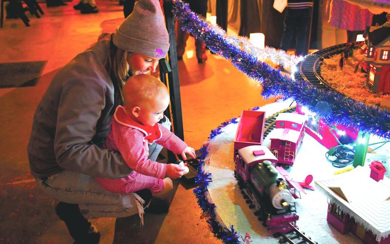 Megan Broome/The Clayton Tribune. Brooke Cannon, chief financial officer of FAITH, shows 9-month-old Holton Morgan the train set at the Christmas Village of Lights display provided by the local nonprofit Fight Abuse in the Home (FAITH) and Kirk Knous earlier this month.