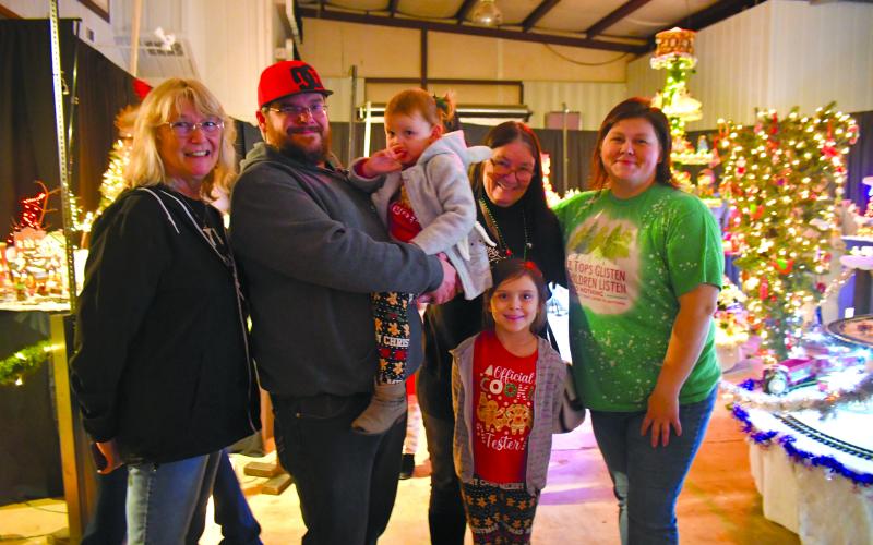 Megan Broome/The Clayton Tribune.  Rosa Hrovat, Kenneth Poole, Fran Poole, Sandie Poole, Ember Poole and Judy Burch are all smiles as they pose in front of the indoor miniature village display at the Christmas Village of Lights last weekend. The event continues on Dec. 16 and 17.