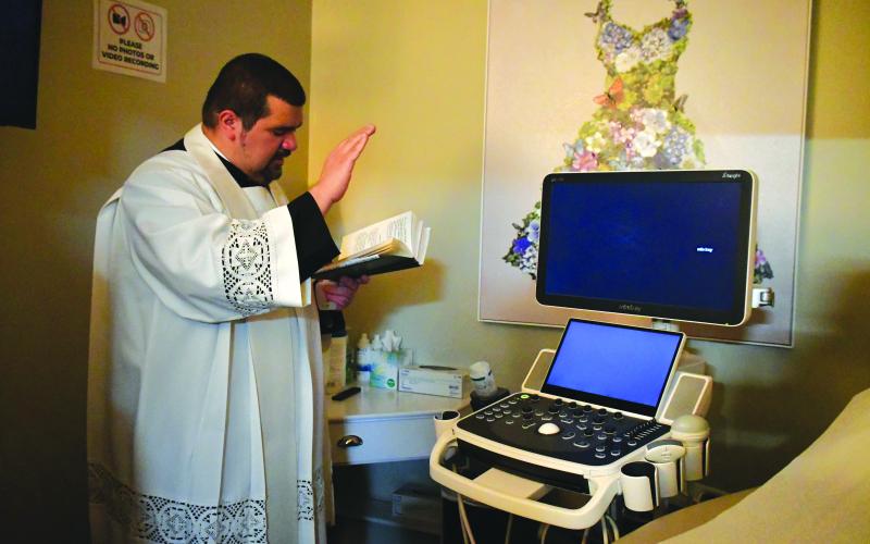 Megan Broome/The Clayton Tribune. Father Luis Alvarez blesses the new ultrasound machine.