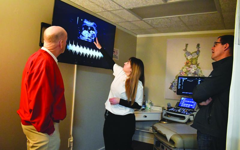 Megan Broome/The Clayton Tribune. Choices Pregnancy Center volunteer Kayla Scott (center) demonstrates the new ultrasound machine at the facility to Eric Vogelbacher (right), Grand Knight for the Knights of Columbus at St. Helena Catholic Church, Choices Advisory Board member and Rotary Club of Clayton member, and Matt Mitcham, Rotary Club member.