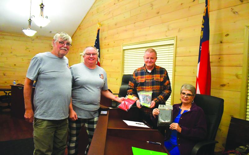 Megan Broome/The Clayton Tribune. Johnnie Robinson, president of the Board of Directors of Creating Ties that Bind, and Pam Wheeler, CEO of Creating Ties That Bind (left) present a United States flag, State of Georgia flag, and POW flag to Tiger Mayor Mike Carnes, center, and the Tiger Town Council at the Feb. 13 council meeting. Also pictured is Tiger Town Council member Karen Lovell.