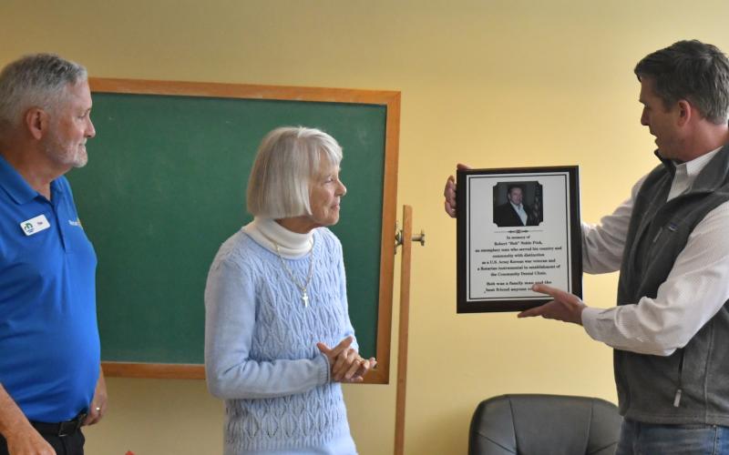 Megan Broome/The Clayton Tribune. Rotarian Tim Ranney, chair of Clayton Rotary Foundation, Inc., (left) presents a memorial plaque for the late Rotarian Robert “Bob” Noble Fink to Fink’s wife Gwen Fink and grandson Robert Fink III during a dedication at the Rabun County Health Department March 10. The plaque is displayed in the lobby of the Community Dental Clinic, established through the Clayton Rotary Foundation, to honor Fink, who was instrumental in establishing the dental clinic.