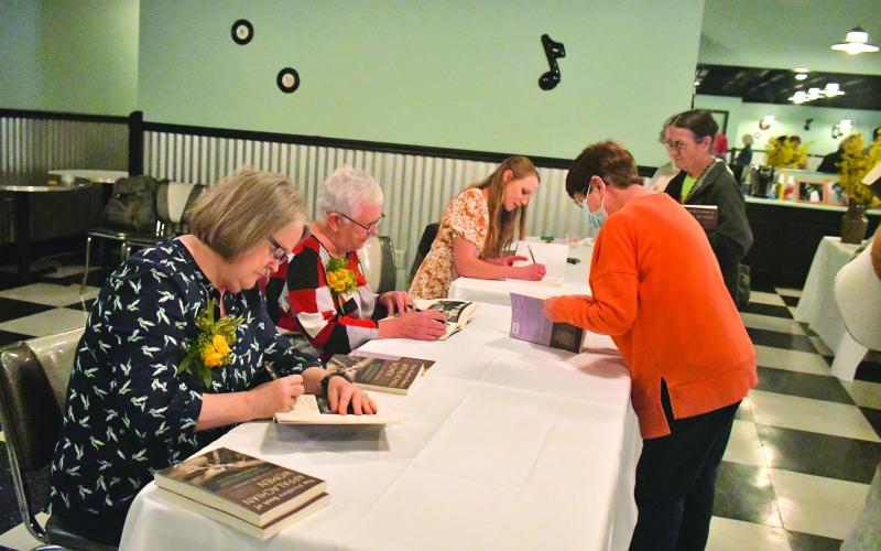 Megan Broome/The Clayton Tribune. Claudia Dodgins (right) has her Foxfire book signed by some of the women featured within the pages. Signing books at the tables are Kaye Carver Collins (left) and Sharon Stiles, both featured; and Kami Ahrens, who wrote and edited the book and is curator and director of Education for Foxfire.