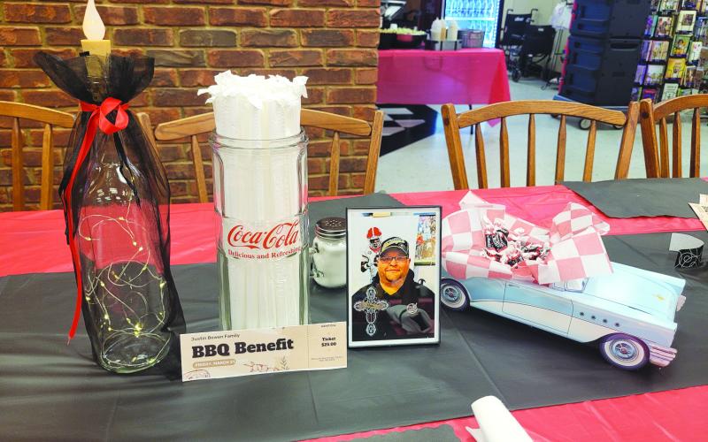Megan Broome/The Clayton Tribune. Tables were decorated with pictures honoring Justin Bowen’s life, candles, model classic cars with trunks filled with tootsie roll candies and lighted display bottles at the BBQ benefit.