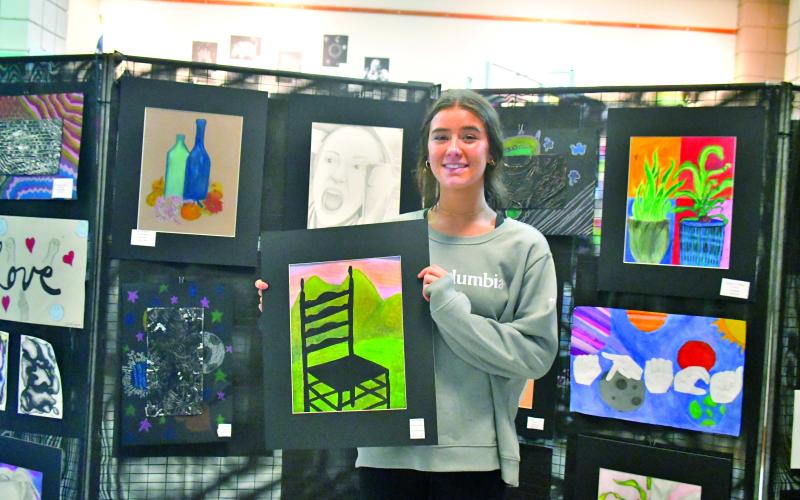 Megan Broome/The Clayton Tribune. Junior Alexis Hopper proudly displays her mixed media art titled “Sunset Chair” at the showcase.