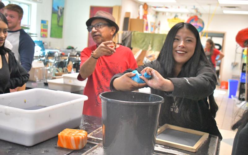 Megan Broome/The Clayton Tribune. Student Camila Gaspar smiles as she hand makes paper with guest artist Javier Silverio onlooking in the Rabun County High School art room April 21. Gaspar squeezes a sponge to make paper just as Silverio does at Taller Leñateros in Chiapas, Mexico.