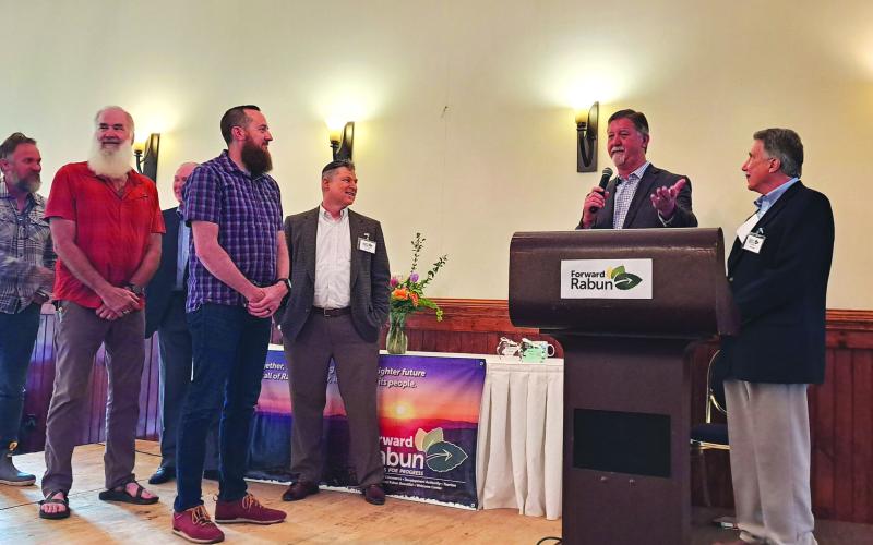 Megan Broome/The Clayton Tribune. Clayton Mayor Kurt Cannon addresses the audience at the May 16 Forward Rabun/Rabun County Chamber of Commerce Community and Business Awards Breakfast. Standing next to Cannon is Rabun County Commission Chairman Greg James and the staff of Outdoor 76. In the background are Rick Story and Tony Penrose, representing Forward Rabun.