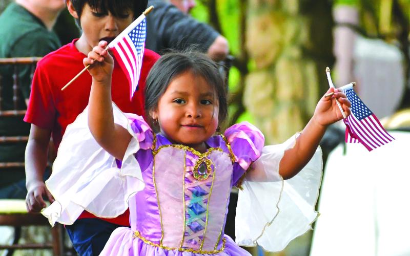 Megan Broome/The Clayton Tribune. Annalia Contreras, 3, waves American Flags in excitement and passes them out to visitors to The Dillard House for the Memorial Day weekend event on the Oaklawn Sunday, May 28. Behind her is her big brother Mateo Contreras, 6.