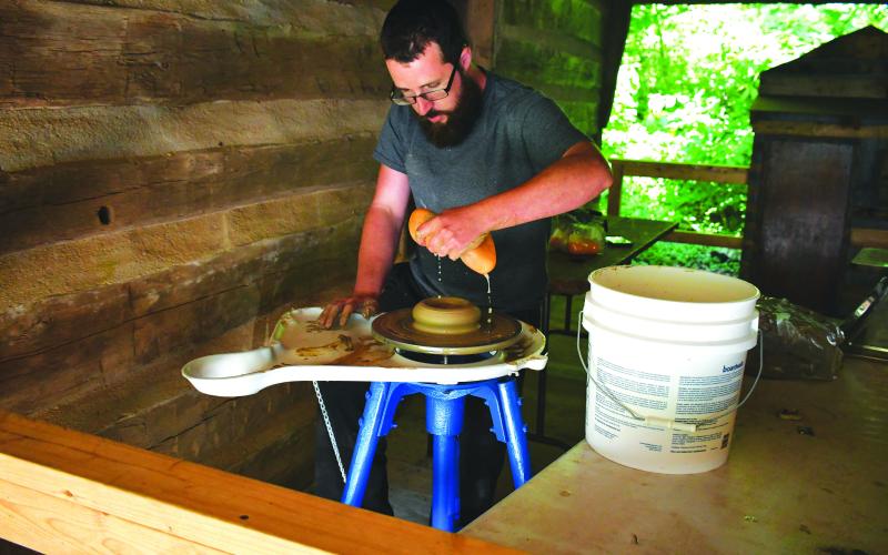Luke Morey/The Clayton Tribune. Daniel Bollinger creates pottery at the annual Foxfire Heritage Days event that was June 9 and 10 in Mountain City.Left: Enoch Autry/The Clayton Tribune. Sisters Anna, 7, and Claire, 4, Miller play inside one of the small Foxfire structures that were built for children.