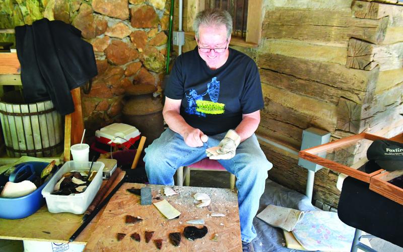 Luke Morey/The Clayton Tribune. At the Heritage Days on June 9, Jim Enloe does some flintknapping at the Mountain City site. Left: Enoch Autry/The Clayton Tribune. Sisters Anna, 7, and Claire, 4, Miller play inside one of the small Foxfire structures that were built for children.