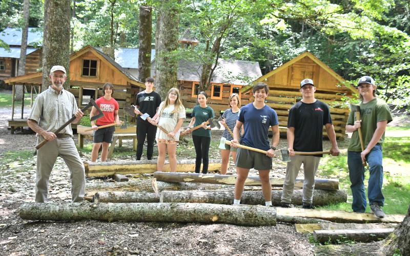 Megan Broome/The Clayton Tribune. Local students participate in the Foxfire Summer Leadership Program and help Foxfire Museum Director Barry Stiles hew logs to prepare building the miniature replica Blacksmith Shop that will be featured at The Children’s Village. Pictured are Stiles; Rabun County High School students Luke Thompson, Sam Flaherty, Celton Littrell, Sean Flaherty, Brinn Justice, and Gavin Sharpe; Rabun Gap-Nacoochee School student Lily Karplus; and home-schooled student Olivia Nixon.