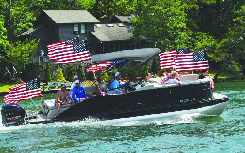 Enoch Autry/The Clayton Tribune. Members of the Ski Patriots wave toward people on balconies of houses on Lake Burton on July 1. In groups, the skiers went around the Rabun County lake for a total of 27 miles. This popular annual event has been putting smiles on individuals’ faces for the past 15 years. This time the youngest skier was 10 years old.