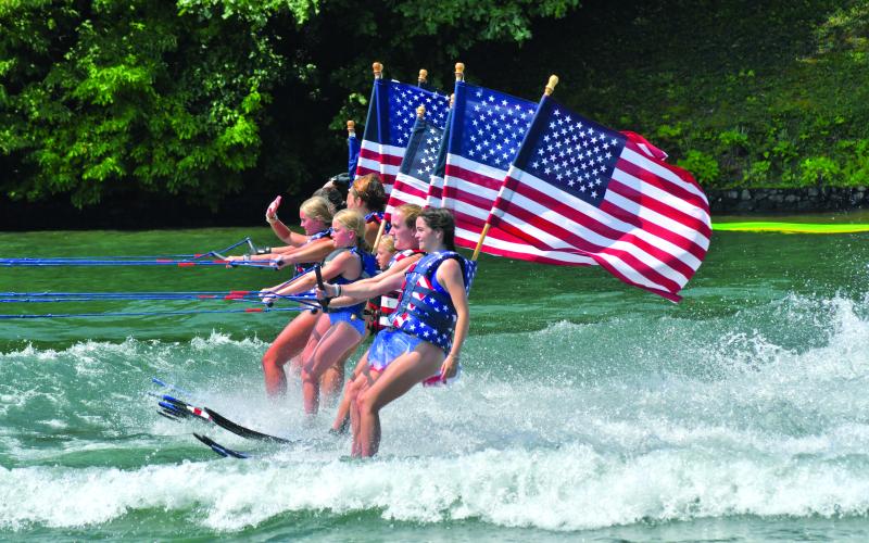 Enoch Autry/The Clayton Tribune. Members of the Ski Patriots wave toward people on balconies of houses on Lake Burton on July 1. In groups, the skiers went around the Rabun County lake for a total of 27 miles. This popular annual event has been putting smiles on individuals’ faces for the past 15 years. This time the youngest skier was 10 years old.