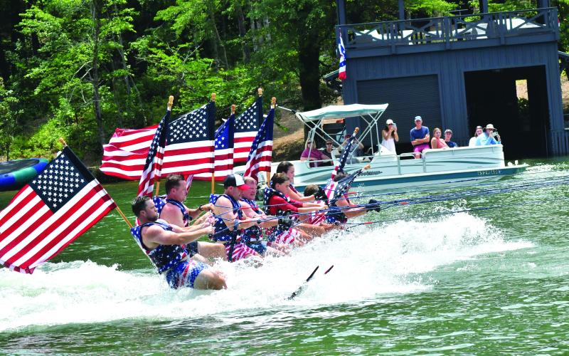 Enoch Autry/The Clayton Tribune. Members of the Ski Patriots wave toward people on balconies of houses on Lake Burton on July 1. In groups, the skiers went around the Rabun County lake for a total of 27 miles. This popular annual event has been putting smiles on individuals’ faces for the past 15 years. This time the youngest skier was 10 years old.