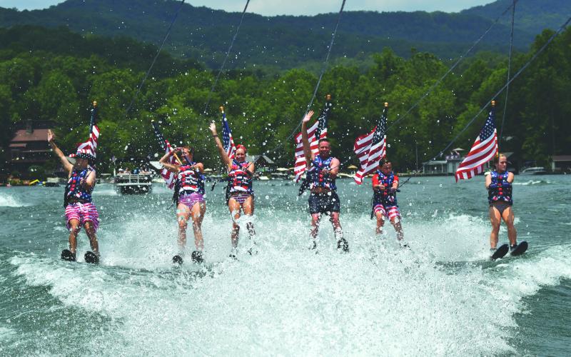 Enoch Autry/The Clayton Tribune. Members of the Ski Patriots wave toward people on balconies of houses on Lake Burton on July 1. In groups, the skiers went around the Rabun County lake for a total of 27 miles. This popular annual event has been putting smiles on individuals’ faces for the past 15 years. This time the youngest skier was 10 years old.