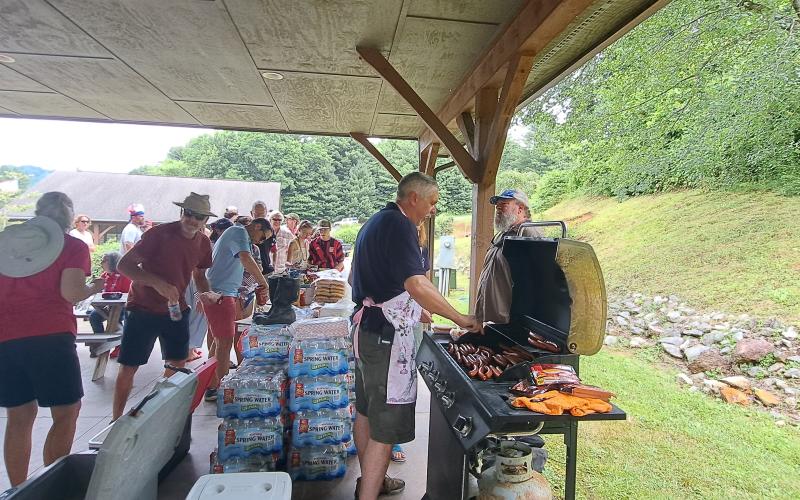 Megan Broome/The Clayton Tribune. Sky Valley-Scaly Mountain Volunteer Fire and Rescue cooked hot dogs for the community during the City of Sky Valley Independence Day activities July 3. Crowds of people showed support. Pictured Fire Chief Ken Sigler grills hotdogs and converses with Sky Valley resident Paul Wheeler.