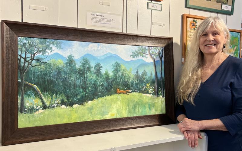 Submitted photo.  Patty Calderone showcases her framed acrylic on canvas painting depicting fox running through a field of greenery at Booth #6 at Butler Galleries on Main Street in Clayton. It is one of two paintings part of a silent auction fundraiser for North Georgia Arts Guild scholarships. The painting is on display at Butler Galleries until July 7 and will be on display for bidding during the Painted Fern Art Festival July 8 and 9.