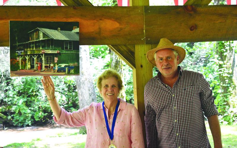 Enoch Autry/The Clayton Tribune. Helen Swain shows her award-winning painting, “Alleys Store 1964,” while standing next to Callaway. Below: James Fairchild of Tiger plays the accordion during the Great American Art Show &amp; Contest on Aug. 5 in Lakemont. In the background are hanging white umbrellas. Other umbrellas were hung around the park area.