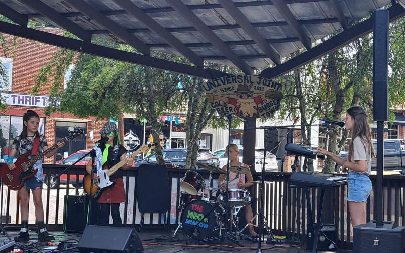 Megan Broome/The Clayton Tribune. The Neon Shadows, an all-girls rock group aged 9-10-years-old, performs a gig at Universal Joint July 16.  The band plays covers and six original songs inspired by their lives titled “Little Ghost,” “Mixed Up,” “Gravity Falls Down,” “Timmy Vibes,” “Reflect the Moon,” and “Surface of the World.”