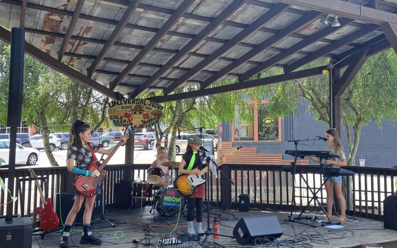Megan Broome/The Clayton Tribune. The Neon Shadows, an all-girls rock group aged 9-10-years-old, performs a gig at Universal Joint July 16.  The band plays covers and six original songs inspired by their lives titled “Little Ghost,” “Mixed Up,” “Gravity Falls Down,” “Timmy Vibes,” “Reflect the Moon,” and “Surface of the World.”
