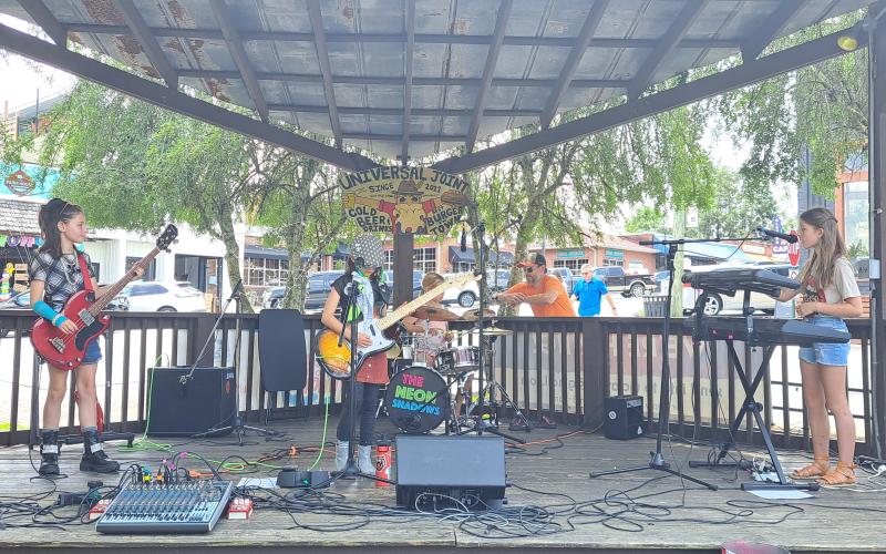 Megan Broome/The Clayton Tribune. The Neon Shadows, an all-girls rock group aged 9-10-years-old, performs a gig at Universal Joint July 16.  The band plays covers and six original songs inspired by their lives titled “Little Ghost,” “Mixed Up,” “Gravity Falls Down,” “Timmy Vibes,” “Reflect the Moon,” and “Surface of the World.”