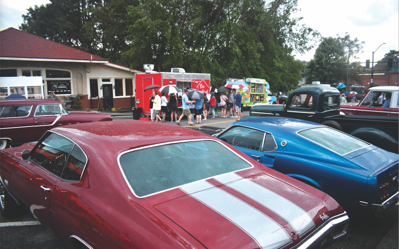 Enoch Autry/The Clayton Tribune. With vintage automobiles parked on Main Street, people bring out umbrellas as the storm arrives.