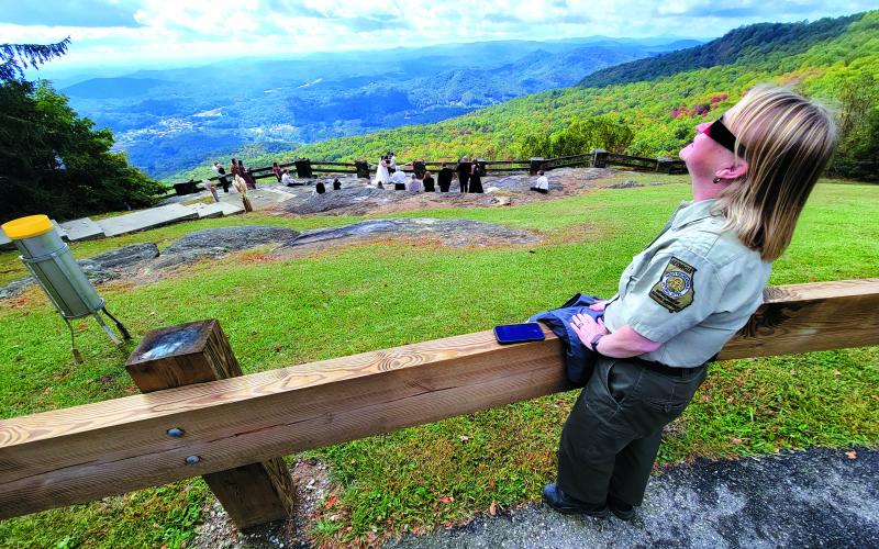 Enoch Autry/The Clayton Tribune. Jessica James-Weeks, the manager of Black Rock Mountain State Park, gazes toward the sky while wearing her special glasses to view the solar eclipse on Oct. 14. In the background, Garrett McClure and Taylor Herrington say their vows in the Blue Ridge Mountains.