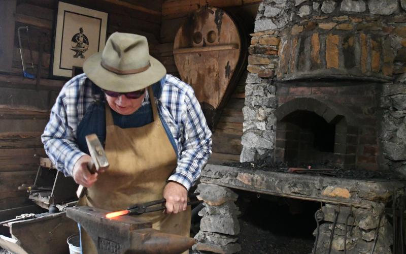 Enoch Autry/The Clayton Tribune. Joe Williams works in the blacksmith shop at Foxfire. Left: Kim Cannon from the Rabun County Public Library read a variety of books that depicted pioneer life in the Appalachian Mountains on the Shooting Creek Cabin porch.