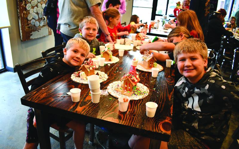 Megan Horn/The Clayton Tribune. Parker Cavender, 10; Easton Cavender, 8; and Holden Cavender, 6, smile as they display their decorated gingerbread houses at the Food Bank Teaching Kitchen event Dec. 13.