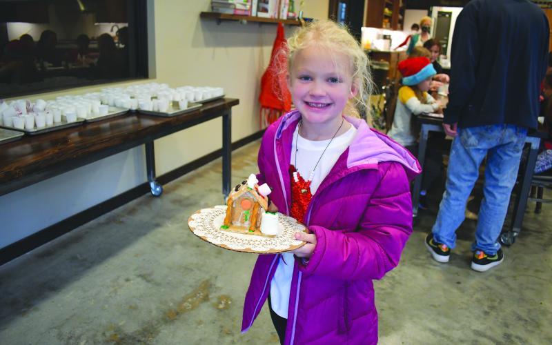 Megan Horn/The Clayton Tribune. Kendall Perteet, 7, shows off her finished gingerbread house that’s decorated with marshmallows, pretzels, Hershey kisses and other sweets.