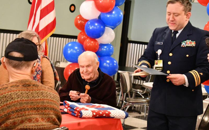 Megan Horn/The Clayton Tribune. Causey smiles as he looks at his Challenge Coin presented to him by Chaplain Dr. Adam Erwin and Carolyn Culpepper with Northeast Georgia Medical Center Hospice and In Home Palliative Care.