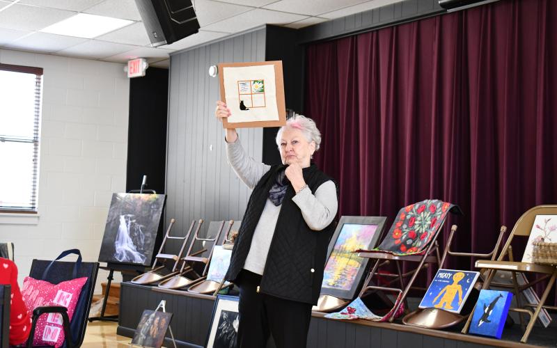 Megan Horn/The Clayton Tribune. Jan Timms shows her artwork depicting a window with four panels and a cat peering through based on the 1954 movie “Rear Window.”