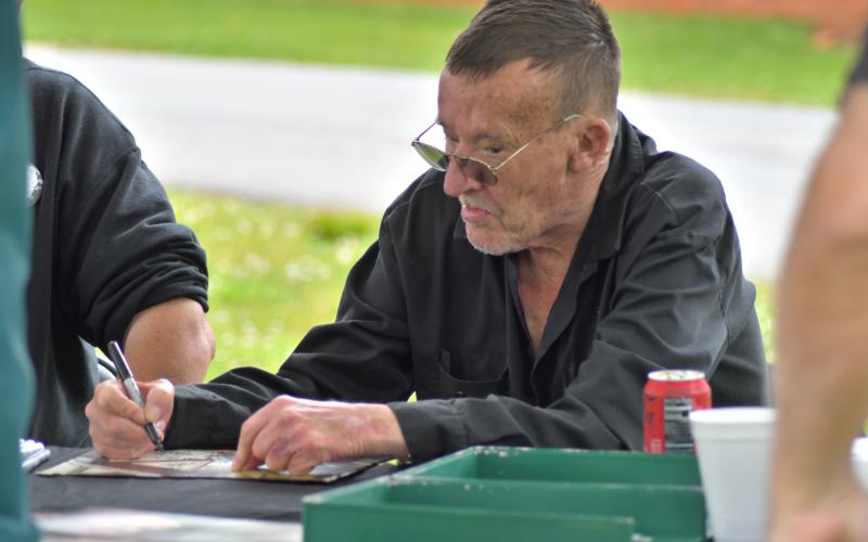 Enoch Autry/The Clayton Tribune. Billy Redden, “Banjo Boy” from the movie “Deliverance,” signs an autograph. Left: John Harrison has to do double take at the bagpipe-playing dinosaur artist Daniel Bollinger.