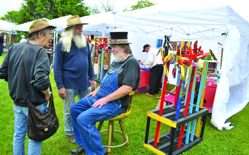 Enoch Autry/The Clayton Tribune. Dinglerfest “Episode 2” to the benefit Sid Weber Memorial Cancer Fund offers plenty of visuals at the R.M. Distillery in Dillard on May 4 as folk artists and visitors dodged rain showers deposited from a day of dark clouds. ABOVE: Pat Garner and Randy Wood talk with event organizer Charlie Dingler. Left: John Harrison has to do double take at the bagpipe-playing dinosaur artist Daniel Bollinger.