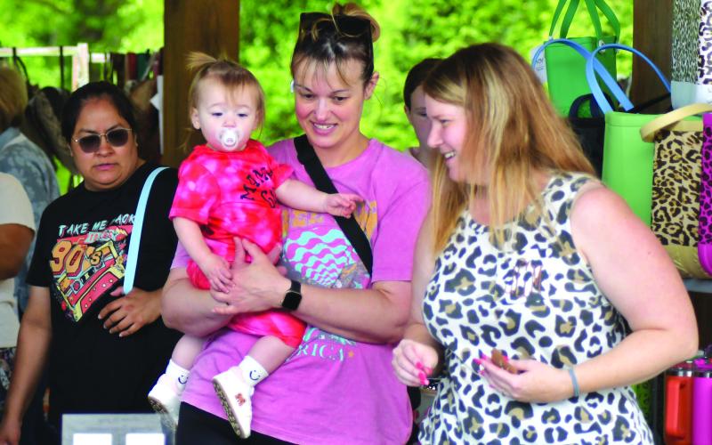 Enoch Autry/The Clayton Tribune.  While shopping with her 15-month-old daughter Uptigrove Kuntz, Mandy Rori talks with vendor Jennifer Craft of Savvy Inspirations at the May 11 Of These Mountains Spring MarketPlace. Craft’s Savvy Inspirations business is from Elberton, Ga.