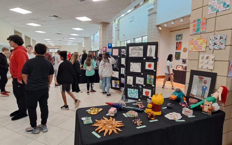 Megan Horn/The Clayton Tribune. Students at Rabun County Schools enjoy colorful artwork created using various mediums by fellow students during the RCMS and RCHS Art Showcase held in the Fine Arts Building May 16. Left: RCHS senior Ryleigh Brotherton displays artwork in red clay titled “Friendly Miner” during the Rabun County High School and Rabun County Middle School Art Showcase held in the Fine Arts Building (FAB) May 16.