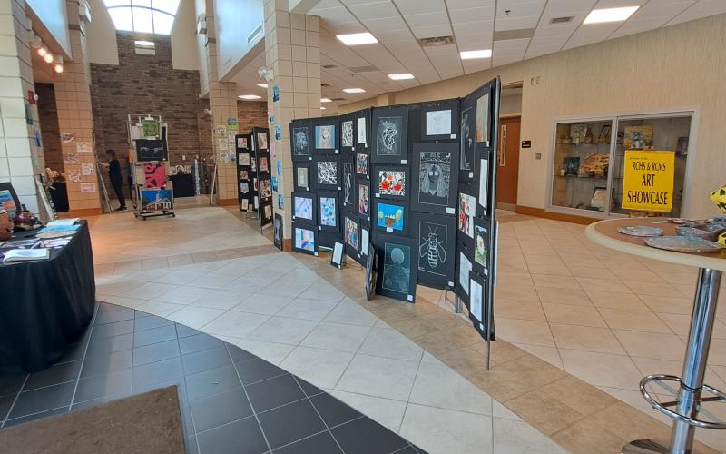 Megan Horn/The Clayton Tribune. Students at Rabun County Schools enjoy colorful artwork created using various mediums by fellow students during the RCMS and RCHS Art Showcase May 16. Left: RCHS senior Ryleigh Brotherton displays artwork in red clay titled “Friendly Miner."