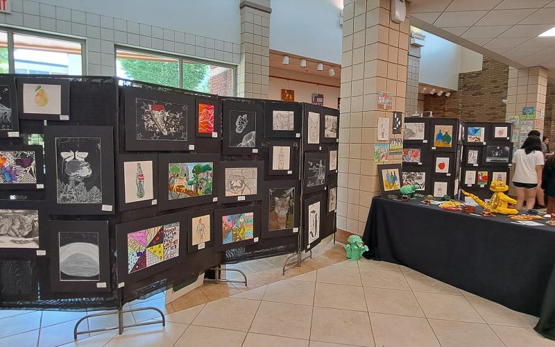 Megan Horn/The Clayton Tribune. Students at Rabun County Schools enjoy colorful artwork created using various mediums by fellow students during the RCMS and RCHS Art Showcase. Left: RCHS senior Ryleigh Brotherton displays artwork in red clay titled “Friendly Miner."