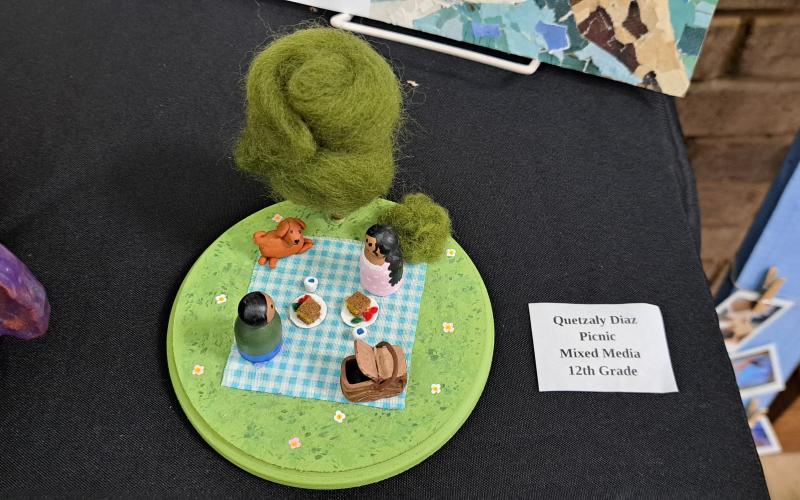 Megan Horn/The Clayton Tribune. Senior Quetzaly Diaz’s mixed media art titled “Picnic” was displayed during the RCMS and RCHS Art Showcase held in the Fine Arts Building (FAB) May 16. Left: RCHS senior Ryleigh Brotherton displays artwork in red clay titled “Friendly Miner."