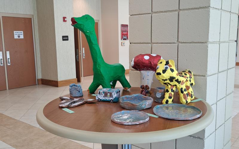 Megan Horn/The Clayton Tribune. Rabun County Middle School students displayed their artwork in the Rabun County Schools Fine Arts Building during the May 16 RCMS and RCHS Art Showcase. Pictured is artwork by Brooklyn Bryson; Delilah Hopkins; Makinsey Huff; Trip McCarthy; and Maclalen Dixon.  Left: RCHS senior Ryleigh Brotherton displays artwork in red clay titled “Friendly Miner."
