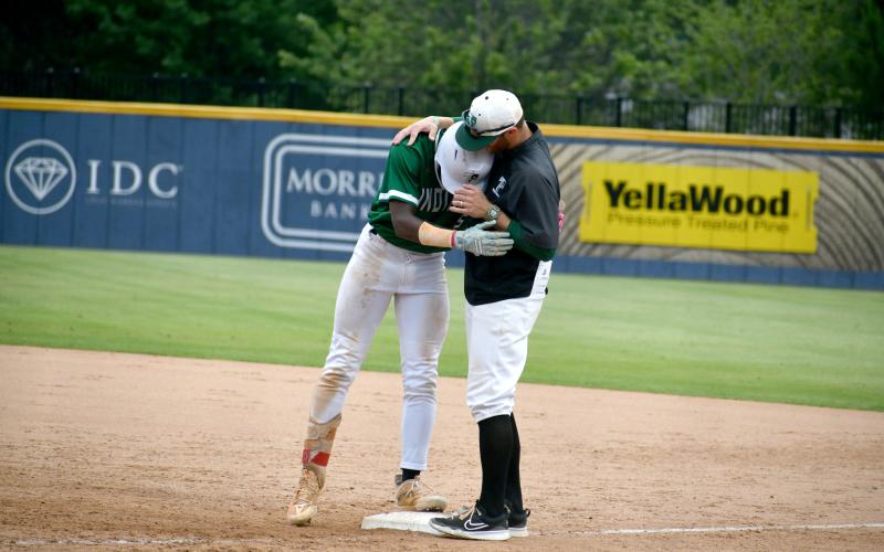 Wade Cheek/The Clayton Tribune. TFS senior Danny Grant hugs assistant coach Nathan Stanley after an RBI single during the Friday, May 17 state baseball championship series against Prince Avenue.