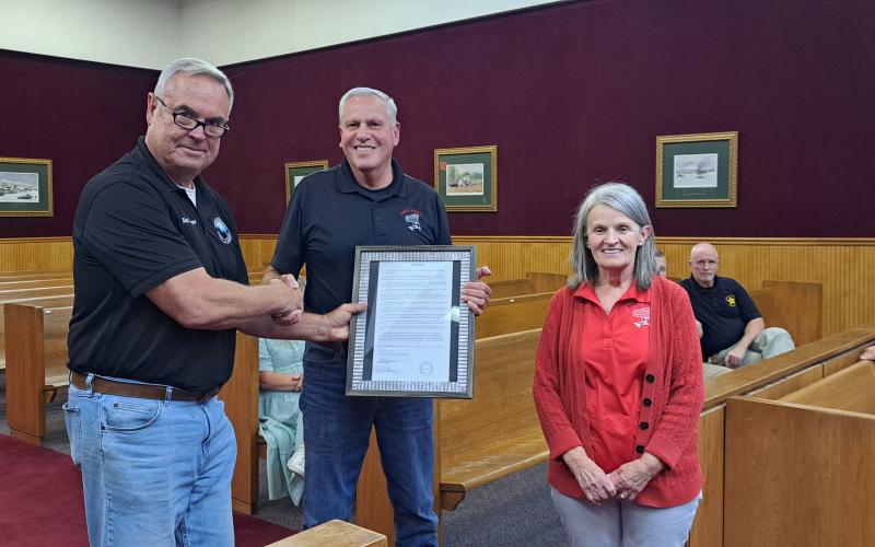 Megan Horn/The Clayton Tribune. Commissioner Kent Woerner, left, presents a Resolution to Andy and Deborah Hunter honoring them for the over 40 years of service that Andy’s Market gave to the community during the May 28 commission meeting. The local grocery store recently closed after decades.