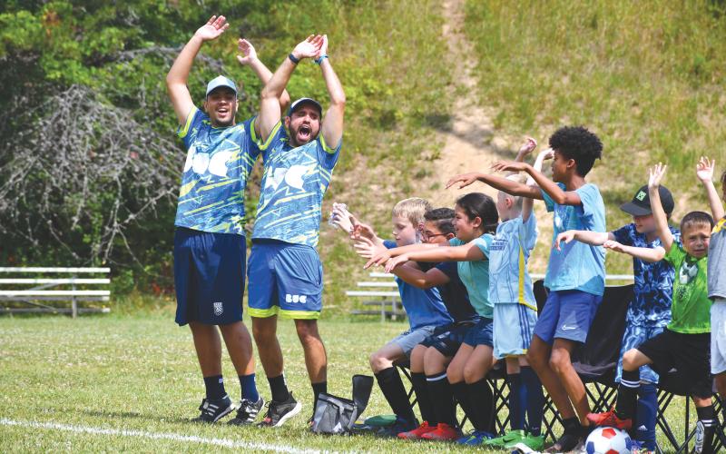 Wade Cheek/The Clayton Tribune. BUC soccer coaches Lucas Padilha and Gabriel Resende celebrate and cheer with local Rabun County kids after a goal during last week’s Brazilian United soccer camp that was held at the Rabun County Recreation Department from June 17-21. ABOVE RIGHT: BUC coach Nathan Nascimente dribbles the ball through youth defenders at this summer’s camp at the Rabun County Recreation Department. The five-day camp allowed campers to learn soccer skills while also having fun with experienced