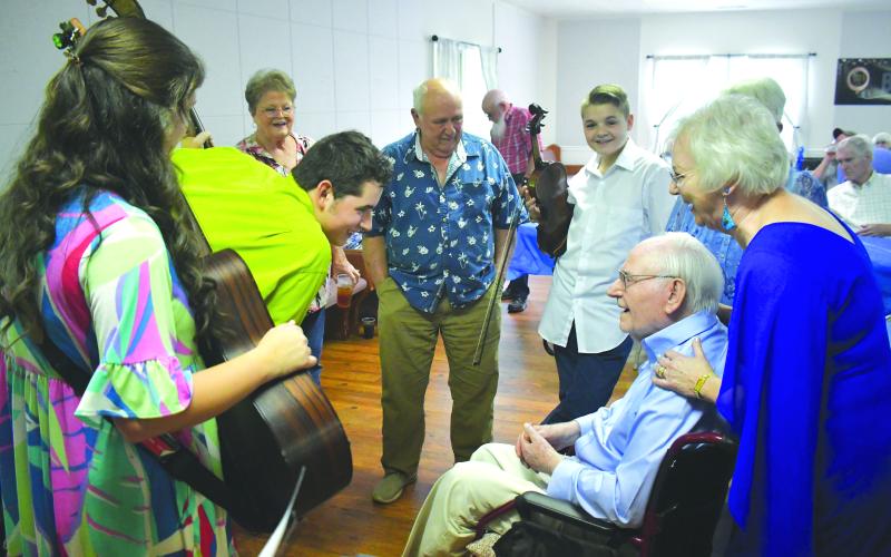 Enoch Autry/The Clayton Tribune. With Laura Chastain standing behind him, 101-year-old Ervin Chastain talks with Bluegrass and Company band members Alyssa White, Elijah Ellenburg and Malachi Ellenburg, and also Beth and Jack Knight at a June 15 birthday celebration at Battle Branch Baptist Church.
