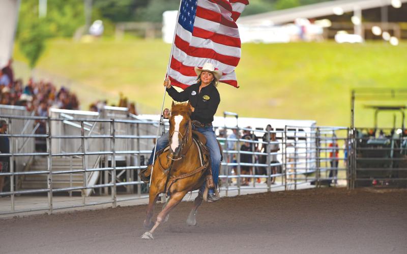 Wade Cheek/The Clayton Tribune. Jamie Ellsworth, a breakaway roper, makes her rounds with the American Flag at Rabun Arena as part of the opening ceremonies of last weekend’s Bar W Rodeo that started on Friday, July 5.