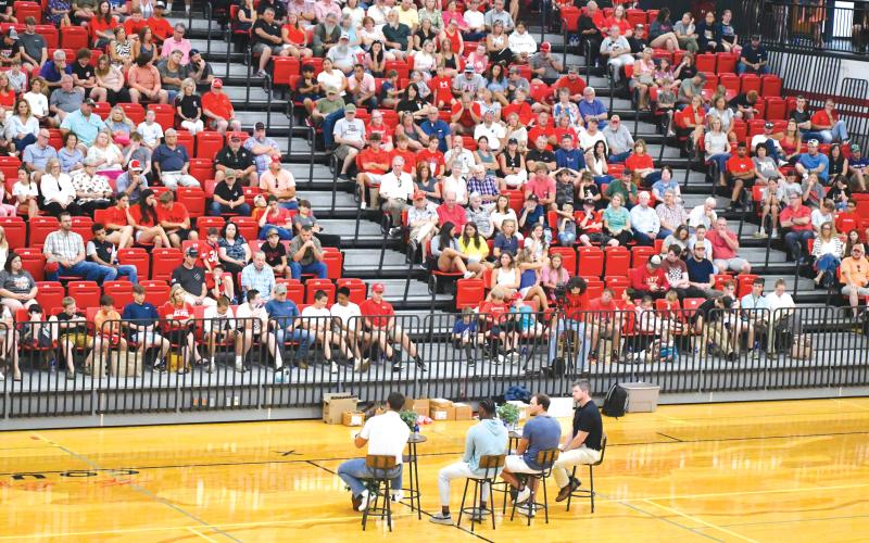 Wade Cheek/The Clayton Tribune. Star football players Charlie Woerner, Gunner Stockton and Malaki Starks sit with Clayton Baptist Church Senior Pastor Joey Thompson on Ken Byrd Court in front of hundreds in the Rabun County High School gymnasium during last Sunday’s Night of Champions on July 14.