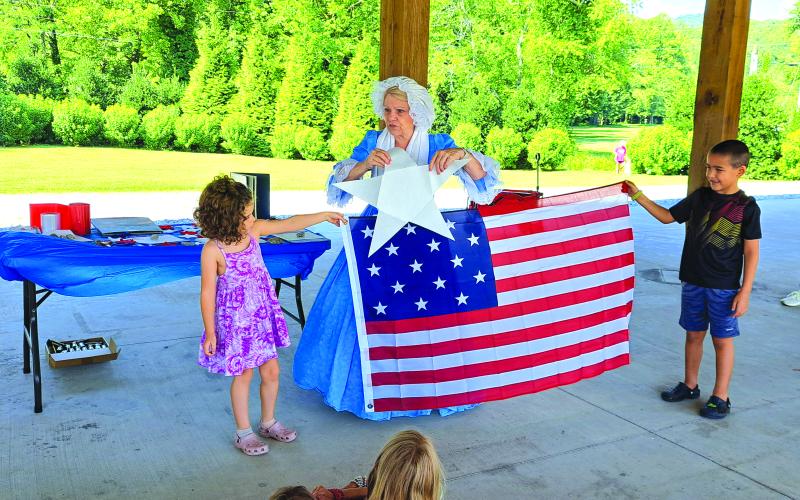 Megan Horn/The Clayton Tribune. Mary Lou Goehring from the Georgia Cameo Society dresses in 1800s fashion and presents a summer reading program describing the events that inspired Francis Scott Key to write the poem that eventually became the National Anthem of the United States of America. Children participate in the demonstration.