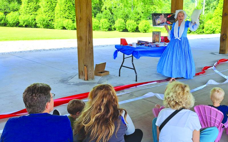 Megan Horn/The Clayton Tribune. Mary Lou Goehring from the Georgia Cameo Society dresses in 1800s fashion and presents a summer reading program describing the events that inspired Francis Scott Key to write the poem that eventually became the National Anthem of the United States of America. Children participate in the demonstration.